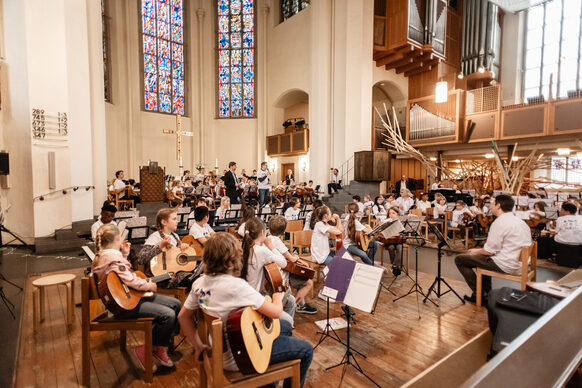 Eine Gruppe von Kindern und Jugendlichen sitzen in einer Kirche und halten Musikinstrumente